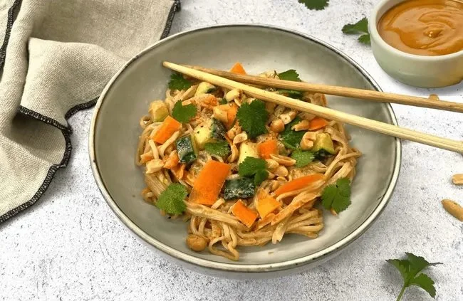 Vermicelles de riz aux légumes et sauce saté dans une assiette colorée