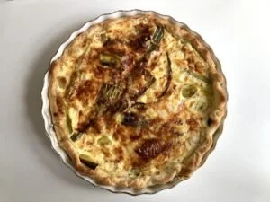 Quiche aux poireaux fraîchement cuite, garnie de légumes verts et d’œufs